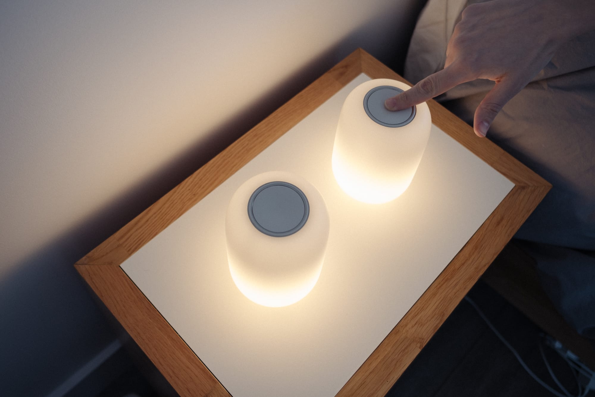 2 lamps on a table, with a female hand pushing the top button on the lamp on the right.