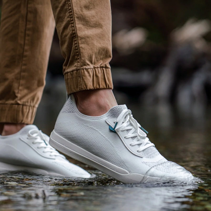 man stepping into water with white vessi shoes
