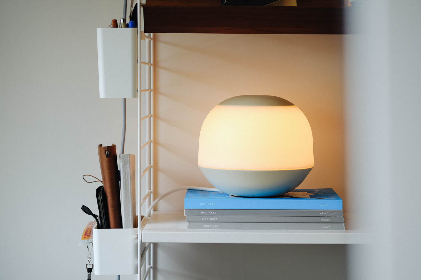 Lamp sitting on a pile of books on a shelf. Books visible.